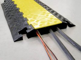 Black rubber cable protector with a yellow flip-top lid, shown with several orange electrical cables running through it.