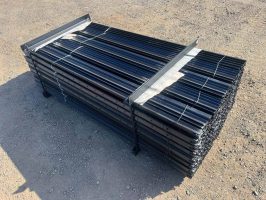 A neatly arranged pile of black steel rods bundled together, resting on a dirt surface.