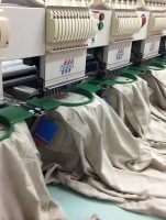 Embroidery machines stitching logos onto light-colored garments in a production setting
